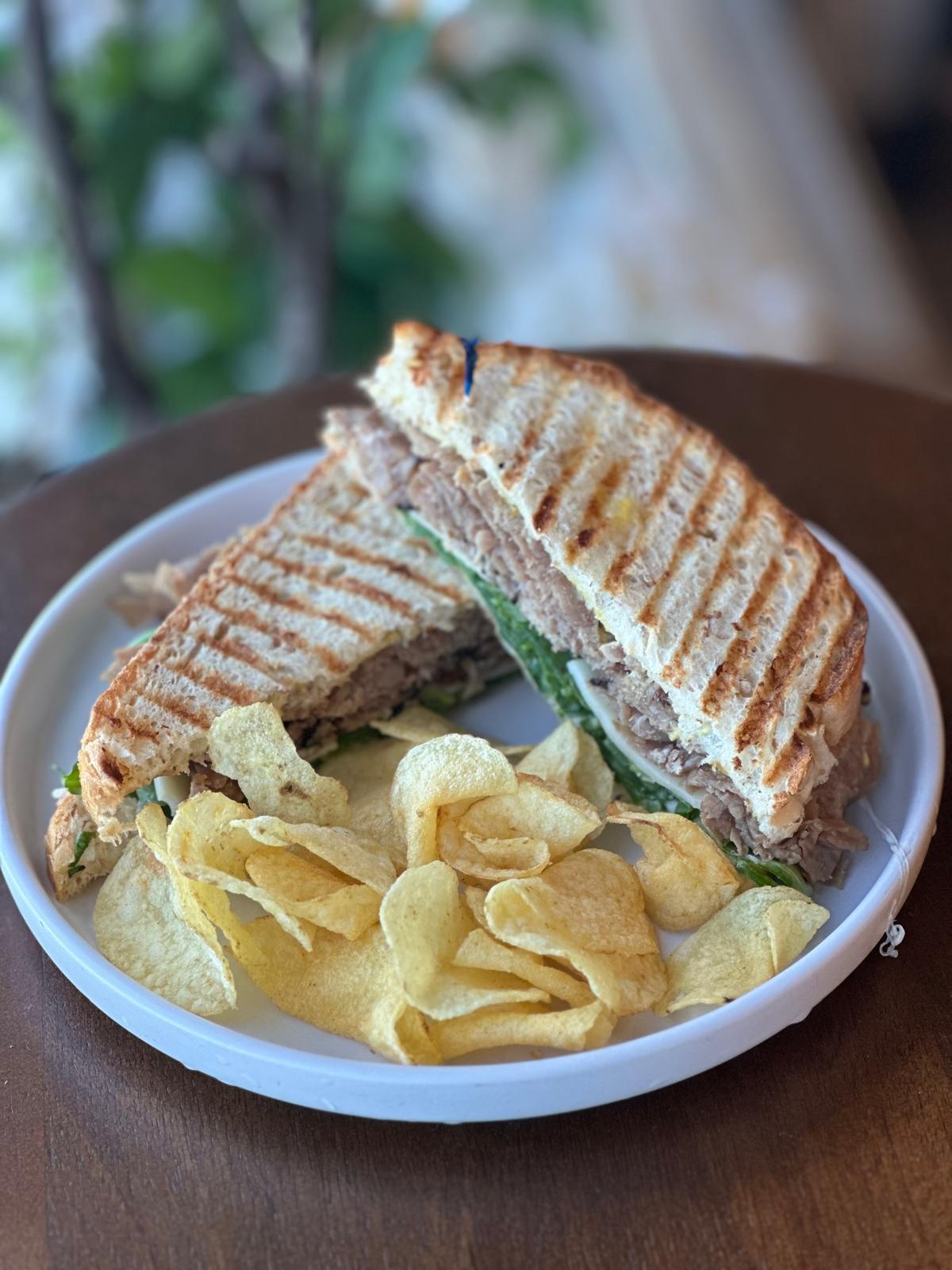 Grilled roast beef arugula sandwich served with potato chips