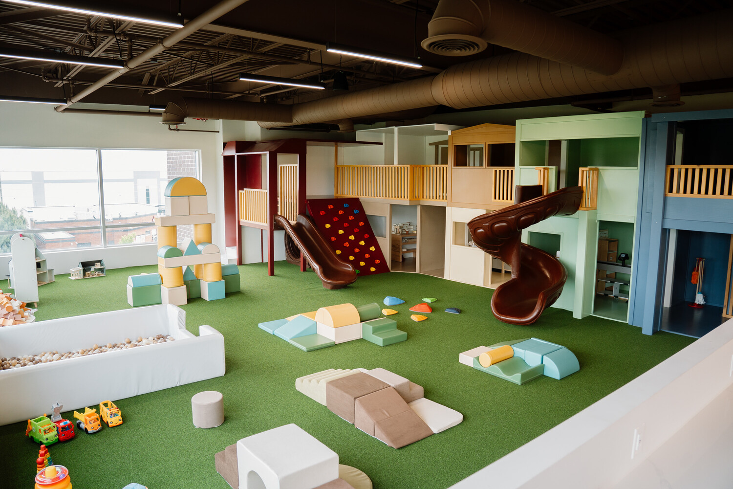 Open toddler play area with wooden playhouses, soft blocks and a spiral slide